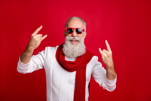 Современный Санта персонаж пожилой человек, показывающий рога тяжелый металл вентилятор носить солнцезащитные очки вязаные одежды изолированный красный фон — стоковое фото