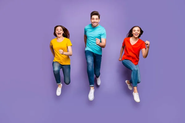 Full length body size front view photo of group of three crazy emotional hipsters models running to you φορώντας κίτρινα μπλε t-shirts απομονωμένο βιολετί φόντο — Φωτογραφία Αρχείου