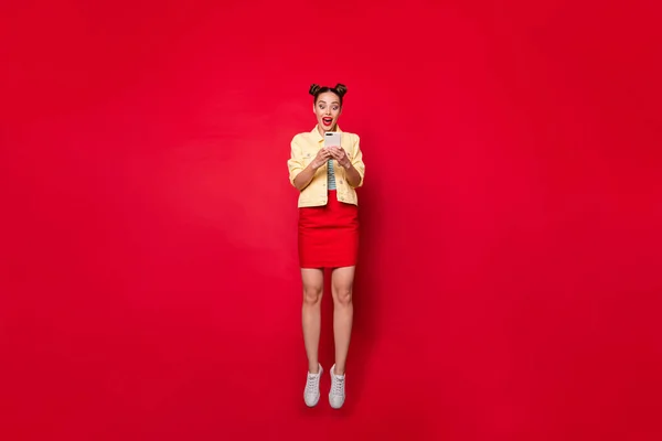 Pełne ciało zdjęcie ładnej skoki pani trzyma telefon ręce nosić casual strój odizolowane czerwone tło — Zdjęcie stockowe