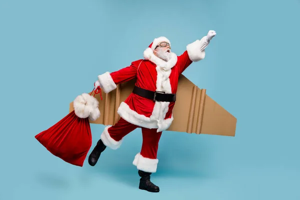 全身上下都是他那漂亮的胖胖的、快乐的、有目的的超级强壮有力的圣诞老人的照片，他身穿飞机机翼，快速运送礼物，提着包，包扎在蓝色的彩色背景上 — 图库照片