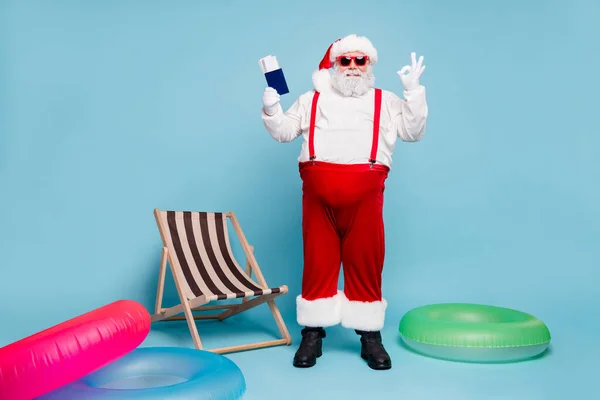 Volledige lengte body size view van mooie vrolijke dikke dikke buik bebaarde Kerstman houden in handen paspoort tickets tonen ok-teken geïsoleerd op blauw turquoise pastel kleur achtergrond — Stockfoto