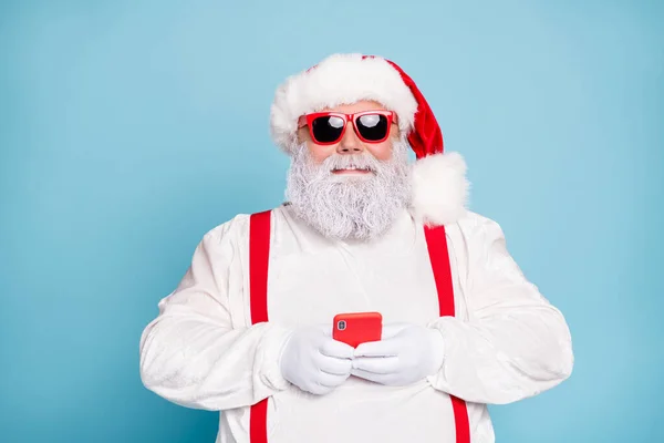 Close-up foto van grappige funky vet wit grijs-harige santa claus gebruik mobiele telefoon type sms gefeliciteerd met noel in blogs dragen overalls rood bretels zonneglas geïsoleerd over blauwe kleur achtergrond — Stockfoto