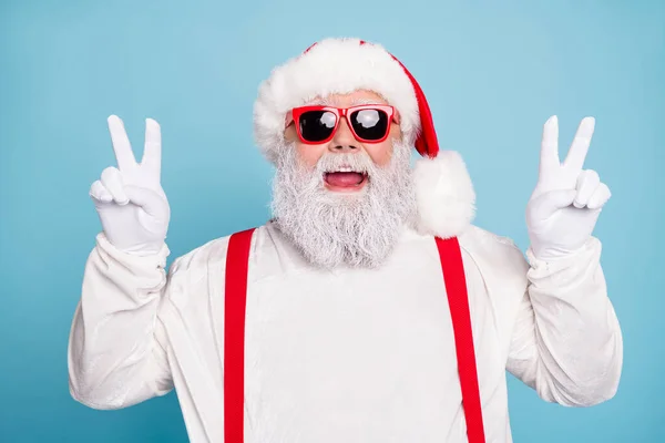 Close-up foto van grappige funky vet santa claus in hipster bril maken v-tekens genieten van kerst noel vakantie dragen witte overall bretels geïsoleerd over blauwe kleur achtergrond — Stockfoto