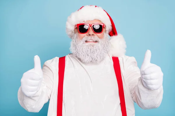Close up foto di divertente funky Babbo Natale in sovrappeso in occhiali moderni mostrano pollice su segno raccomandare x-mas stagione vendite indossare tute bianche bretelle rosse isolato su sfondo di colore blu — Foto Stock