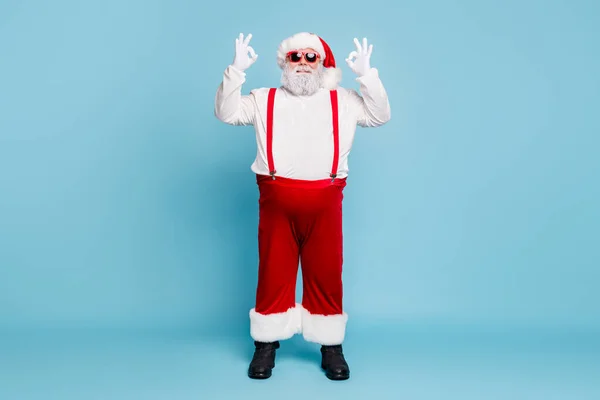 Foto de longitud completa de la grasa divertido padre de Navidad funky con el abdomen del vientre grande muestran signo ok recomiendan descuentos de compras temporada de invierno usan gafas rojas overol aislados sobre fondo de color azul — Foto de Stock