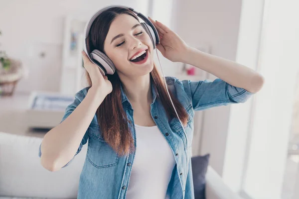 Foto de la increíble dama de buen humor escuchando melodía favorita en las orejeras modernas alegres ojos de cierre con pantalones vaqueros ropa apartamento interior — Foto de Stock