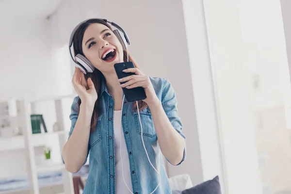 Foto av söt dam med telefon i händerna öronlappar på öron inspelning hem singel för musik studio står nära soffan bär jeans kläder lägenhet inomhus — Stockfoto