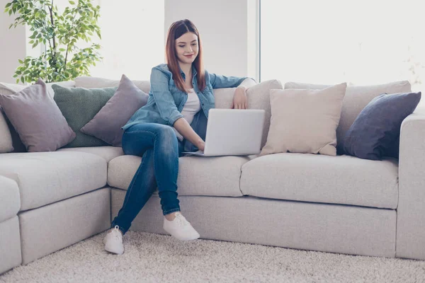 Foto de una mujer de negocios sosteniendo un cuaderno trabajando en casa hablando skype con sus colegas sentados en el sofá usando un apartamento de jeans en interiores —  Fotos de Stock