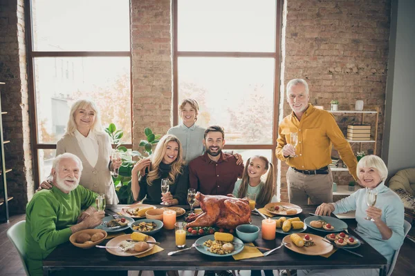 Photo of big family sitting hugging feast table holiday roasted turkey making portrait eight relatives wife husband multi-generation raise wine glasses in living room indoors