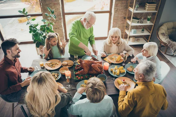 Foto de gran familia sentarse mesa de platos de banquete alrededor de pavo asado abuelo mayor haciendo rebanadas familiares hambrientos esperando emocionados en la sala de estar en el interior —  Fotos de Stock