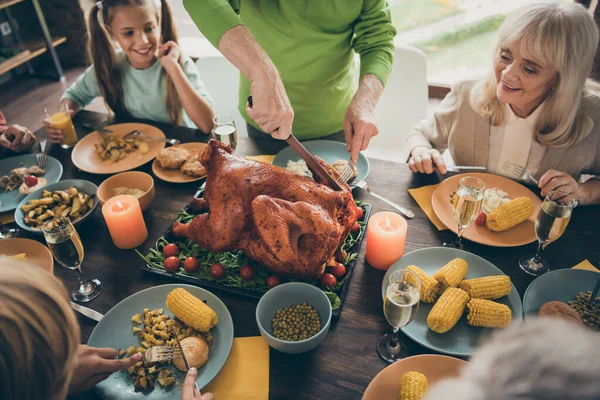 Przycięte zdjęcie pełnej rodziny siedzieć uczta naczynia stół wokół pieczonego indyka dziadek krojenie mięsa na plastry głodnych krewnych czeka podekscytowany w salonie w pomieszczeniach — Zdjęcie stockowe