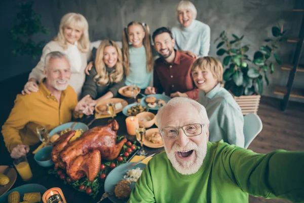 Foto de familia grande sentarse abrazando platos de fiesta mesa alrededor de pavo asado parientes de varias generaciones de pelo gris abuelo haciendo selfies de grupo en la sala de estar en el interior —  Fotos de Stock