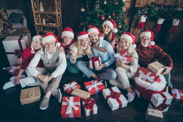 Güzel, neşeli, büyük, aile babası kardeş şapkalı çiftlerin portresi yerde oturmuş, V-işareti Noel günü geleneğini, dekore edilmiş çatı katı tarzı iç mekan dekorasyonunu gösteriyor. — Stok fotoğraf