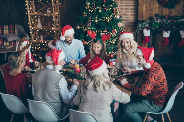 クリスマスの夜の座席の家族の再会食べるにはx-マスの伝統を持っているシニア男は小さな孫娘の笑いはトナカイのヘッドバンドサンタクラスキャップ帽子を身に着けています家の中でノエルな雰囲気 — ストック写真