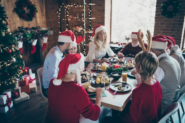 Küçük çocuklarla mutlu noel aile toplantısı. Yetişkin emekliler. Noel ziyafeti masasında Noel Baba şapkalı geyik boynuzu takıyorlar. — Stok fotoğraf