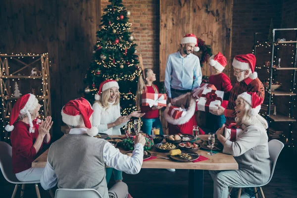 Mutlu noeller, küçük çocuklar, olgun emekliler Noel yemeği masasında Noel Baba şapkalı adam çantalı adam, yeni yıl süslemeleri ile evde hayaller kuruyor. — Stok fotoğraf