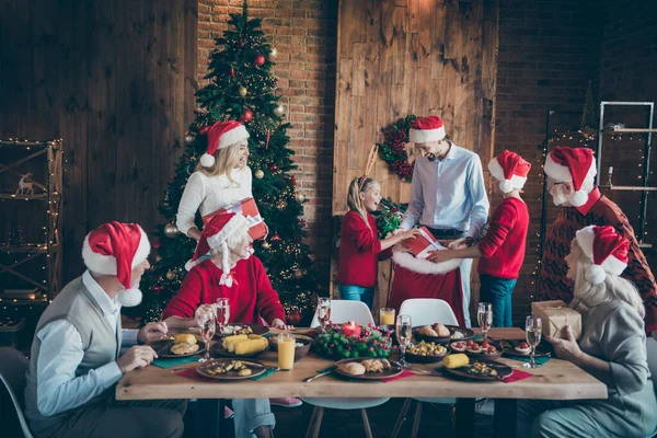 Foto de familia de armonía completa reuniendo mesa de cena compartiendo regalos de x-mas sacando un gran paquete de santa caja de regalo roja en la sala de estar decorada con árbol de x-mas en el interior — Foto de Stock