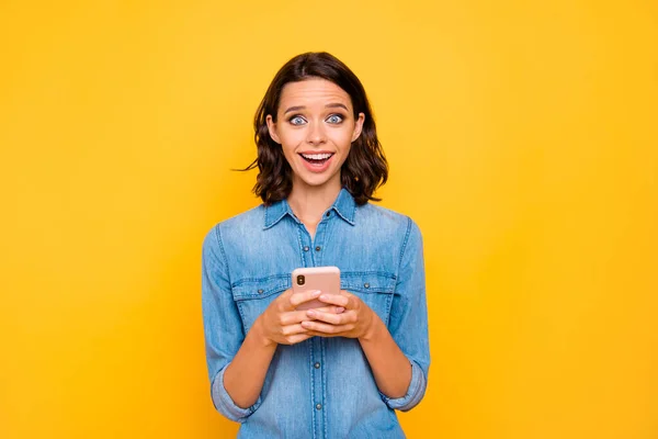 Portret van opgewonden meisje gebruik maken van haar smartphone sms-type post op het sociale netwerk schreeuwen wow omg slijtage denim jeans shirt geïsoleerd over gele kleur achtergrond — Stockfoto