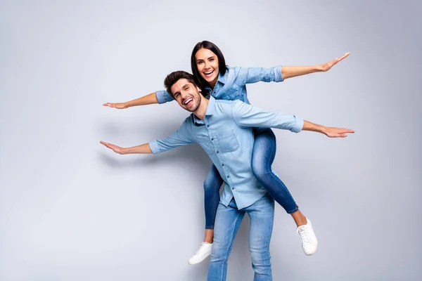 Foto de cool pair en el amor chico sosteniendo lady piggyback pretendiendo avión vuelo extendido manos como alas desgaste casual jeans ropa aislado gris color fondo — Foto de Stock