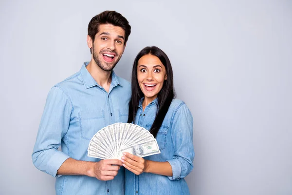 Foto de dos personas abrazadas juntas sosteniendo el dinero que han ganado en la lotería usando jeans denim aislado fondo de color gris — Foto de Stock