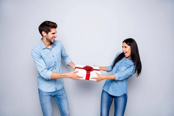 Foto de alegre elegante casal branco da moda de duas pessoas juntos contestando sobre quem vai obter a caixa de presente vestindo jeans jeans isolado sobre fundo de cor cinza — Fotografia de Stock