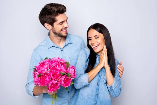 Фото красивої милої пари з двох чоловік дівчина радіє з отриманням букета квітів фуксії і хлопець обіймає її ззаду в джинсах джинсовий ізольований сірий кольоровий фон — стокове фото