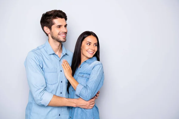 灰色の背景に隔離されたジーンズのシャツを身に着けている空の空白のスペースを離れて見ている人々の魅力的な陽気なかわいいカップルの写真 — ストック写真