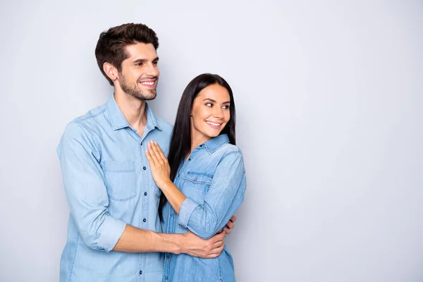 Foto van charmante vrolijke schattige leuke paar mensen kijken weg naar lege lege ruimte dragen jeans shirts knuffelen geïsoleerd over grijze kleur achtergrond — Stockfoto