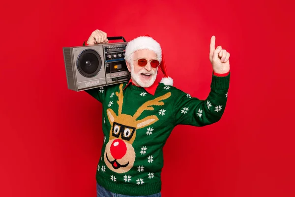 Bild av äldre rolig Santa man hålla vintage bandspelare kylning på ung fest länge väntat gäst bära specifikationer x-mas ful prydnad tröja mössa isolerad röd bakgrund — Stockfoto