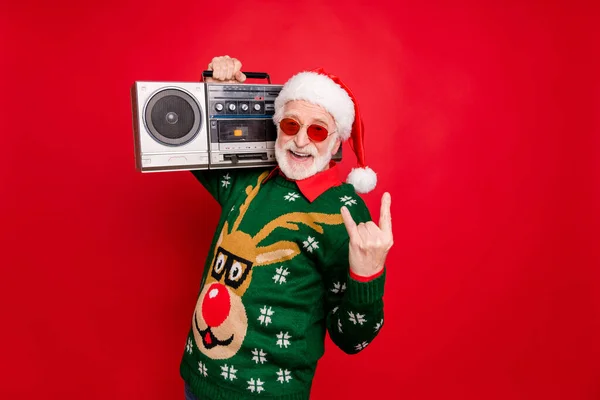 Bild av äldre rolig Santa man håller vintage bandspelare på ung fest visa horn bära sol specs x-mas ful prydnad tröja mössa isolerad röd bakgrund — Stockfoto