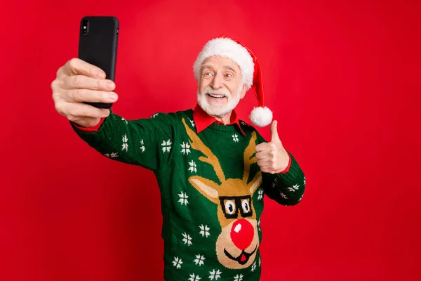 Bild av Santa man som håller telefon gör selfies för x-mas blogg höja tummen upp uttrycka cool attityd bära x-mas ful prydnad tröja mössa isolerad röd bakgrund — Stockfoto