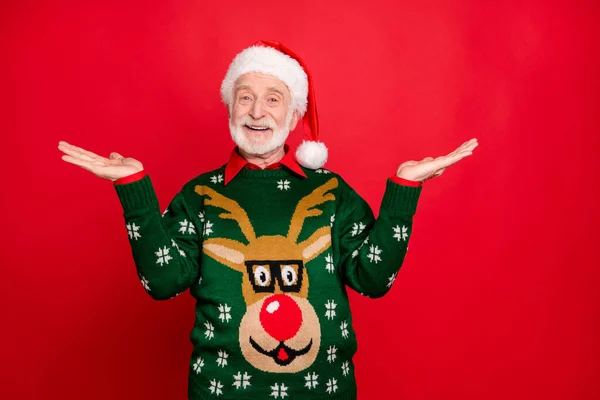 Photo of santa senior man holding sale products on open palms advising low holiday prices wear x-mas ugly ornament sweater isolated red background — Stock Photo, Image