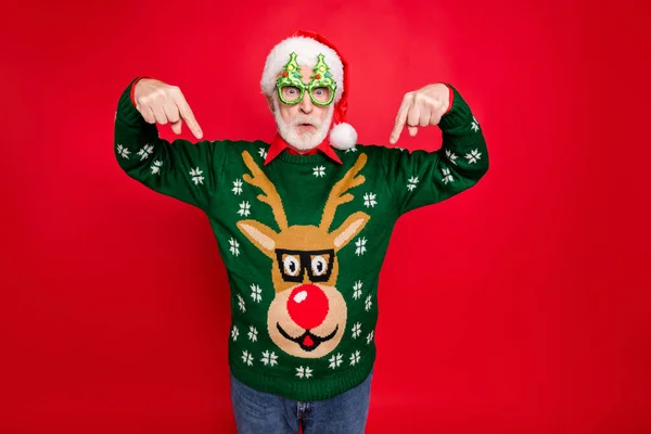 Foto av Santa tittar på låga julen shopping priser indikerar fingrar på billiga jumper bär x-mas träd form specs ful prydnad tröja isolerad röd bakgrund — Stockfoto