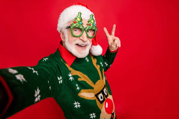 Närbild foto av roliga åldrade Santa claus roll man gör selfies visar v-tecken symbol bära x-mas träd form specs ful prydnad tröja isolerad röd bakgrund — Stockfoto