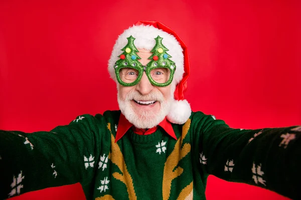 Foto de primer plano de divertido anciano papel de santa claus hombre haciendo selfies locos desgaste x-mas árbol forma especificaciones jersey de punto sombrero aislado fondo rojo —  Fotos de Stock