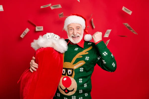 Bild av gråhårig Santa far håller stora gåvor säck full av pengar firar dollar kontanter faller bära ful prydnad ren tröja isolerad röd bakgrund — Stockfoto