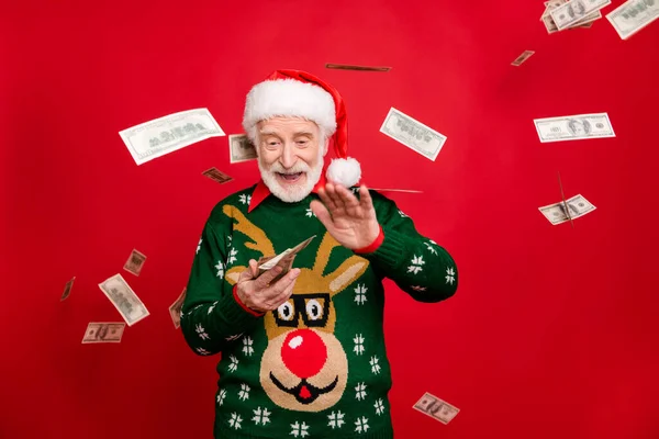 Ritratto di divertente funky pazzo grigio bianco capelli barba vecchio uomo indossare cappello di Babbo Natale corna disegno maglione gettare cashback reddito ha vinto in x-mas lotteria isolato colore rosso sfondo con soldi cadere volare — Foto Stock