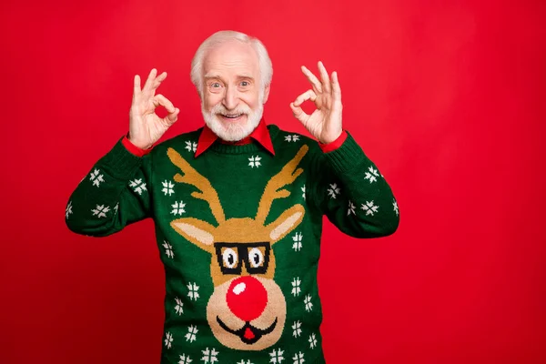 Portrait of cool positive old man show okay sign recommend winter season tradition discounts wear trend pullover with reindeer pattern decor isolated over red color background — Stock Photo, Image