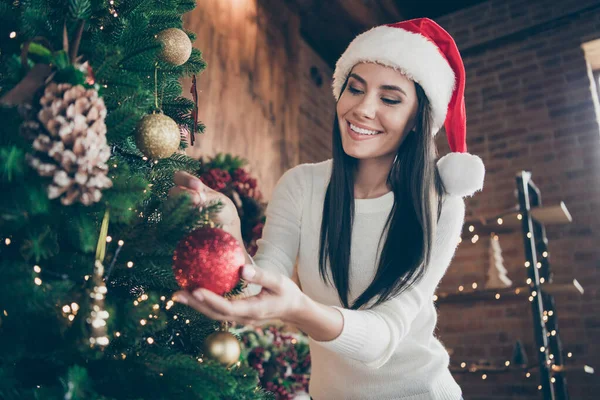 Portré pozitív vidám lány Santa Claus fejfedő lógni karácsonyi labda örökzöld fa az x-mas újévi ünnepség a házban ünnepi advent dekoráció dísz beltéri — Stock Fotó