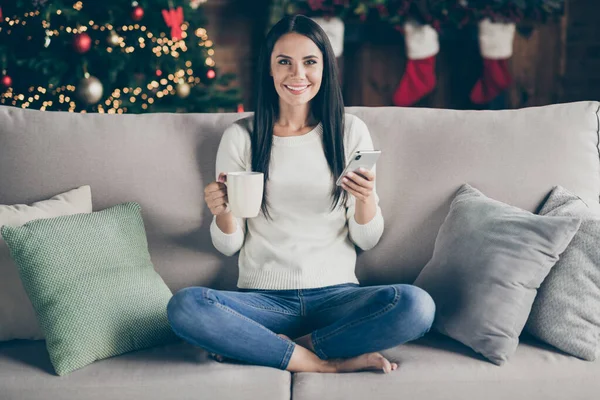 원문 기사보기 긍정적 인 여성 이 편 안 한 소파에 앉아 있는 모습 성탄절 분위기를 즐기고 있는 가운데, 휴대 전화를 사용하여 겨울 할인을 구매 한다. — 스톡 사진