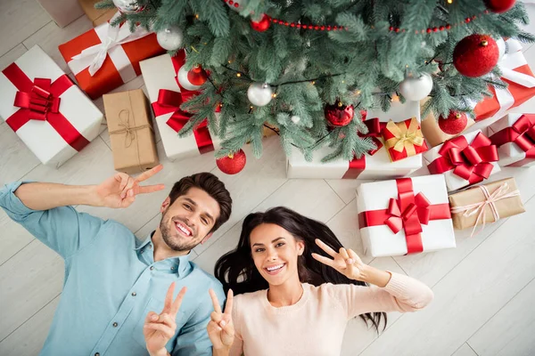 Top alta foto de duas pessoas adoráveis com cabelo morena deitado no chão branco com giftboxes fazendo v-sinais desfrutando Natal tempo x-mas feriados em casa dentro de casa — Fotografia de Stock
