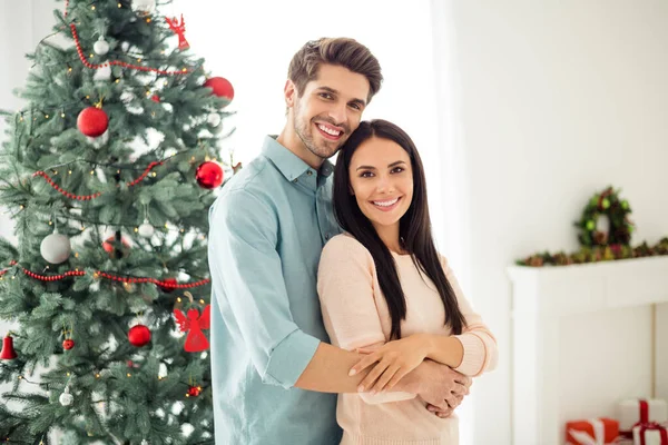 ブルネットの髪の抱擁を持つ2人の魅力的なカップルの肖像画は、屋内で新年の装飾花輪で家の中でクリスマスの時間のクリスマスの休日を楽しむロマンスを感じる — ストック写真