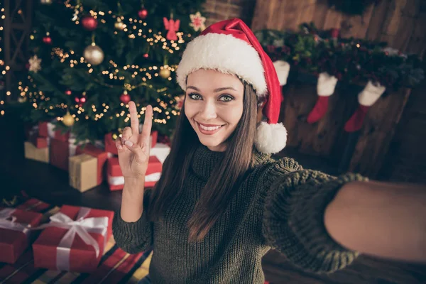 Close up foto do blogueiro positivo ano novo morena cabelo menina em pulôver tricotado tirar selfie fazer v-sinais na árvore evergreen natal com muitas caixas de presente desgaste santa claus cap em casa dentro de casa — Fotografia de Stock