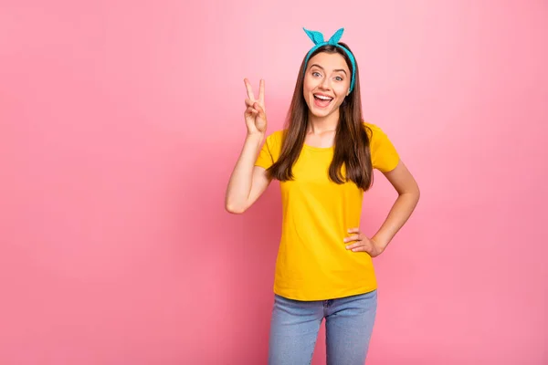 Портрет прекрасної молоді, яка сміється над рожевим тлом, роблячи v-знаки в жовтій футболці — стокове фото