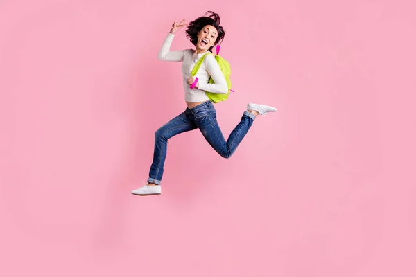 Foto de corpo inteiro de senhora pulando alta segurando mochila verde correndo para fazer compras mostrando v-sinal pulôver desgaste e jeans isolado cor rosa fundo — Fotografia de Stock