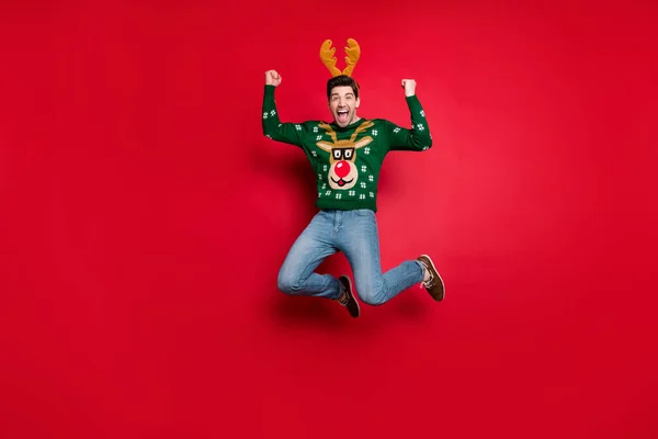 Ganzkörper-Foto von flippigen Kerl springen hoch aufgeregt mit x-mas Rabatte tragen gestrickten grünen Pullover mit hässlichen Hirsch Ornament isoliert roten Farbhintergrund — Stockfoto