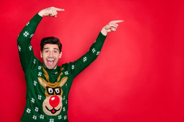 Foto di ragazzo bello emotivo che indica le dita sul banner di vendita x-mas indossare pullover verde lavorato a maglia alla moda con cervo isolato sfondo di colore rosso — Foto Stock