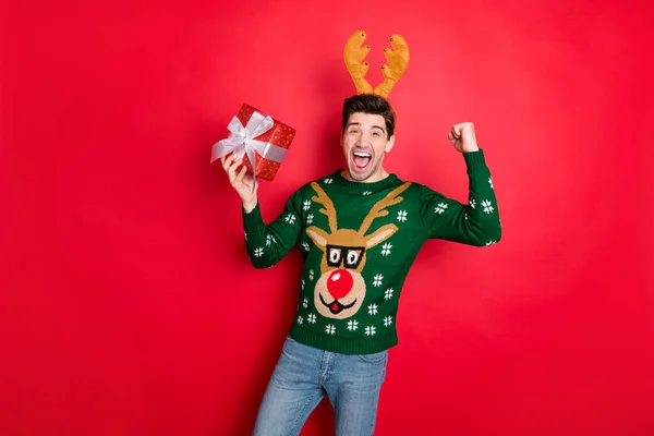 Portrait of his he nice attractive overjoyed cheerful cheery guy wearing deer sweater holding in hand gift rejoicing isolated over bright vivid shine vibrant red color background — ストック写真