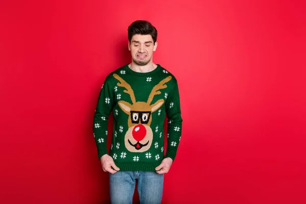 What a disgust. Portrait of frustrated man look at his funny ugly sweater dislike his christmas present wear denim jeans isolated over red color background — Stock Photo, Image