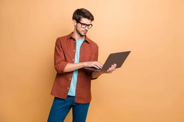 Portret jego ładne atrakcyjne poważne sukcesy inteligentne inteligentne skupione brunetka facet trzyma w ręce laptop przeglądanie izolowane na beżowy kolor pastelowe tło — Zdjęcie stockowe